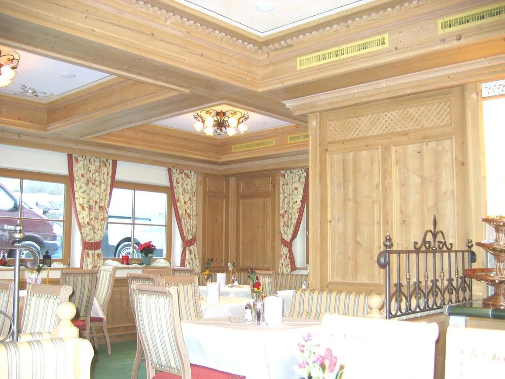 Hotelrestaurant mit Kassettendecke und Wandvertäfelung aus hellem Holz, gedeckten Tischen und Vorhängen mit Blumenmuster