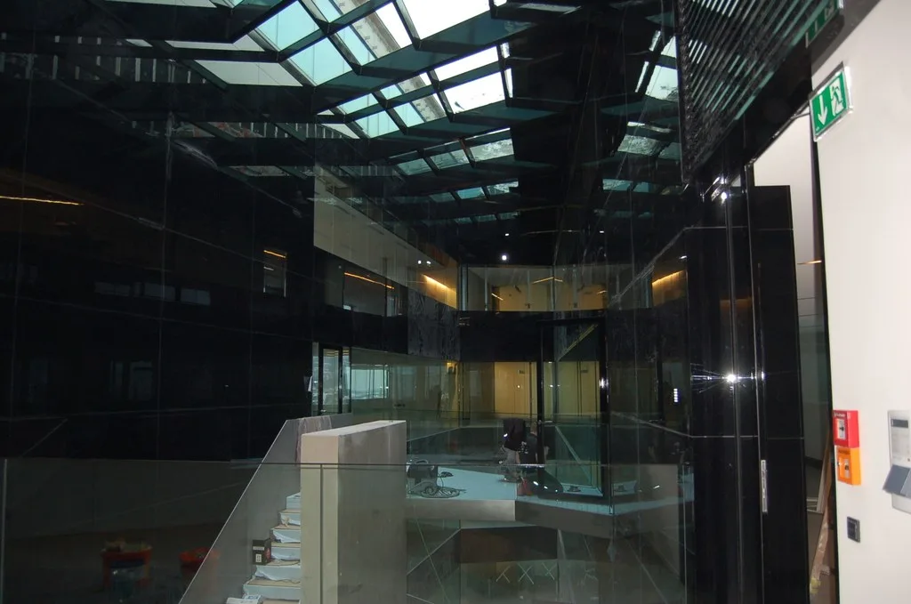 Atrium mit Glasdach, schwarzen Glasflächen und Glasbrüstungen an einer Treppe, noch im Ausbau