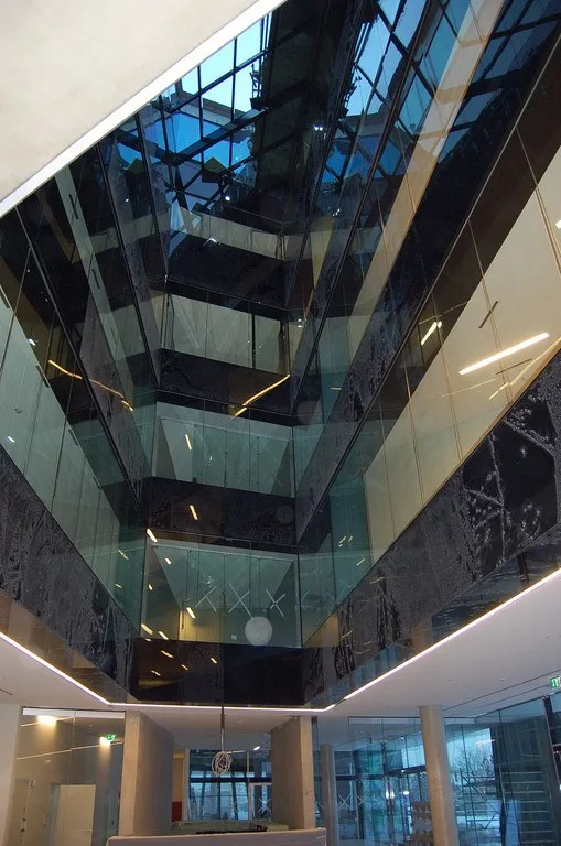 Blick nach oben in einen Lichthof mit dunklen Glasbrüstungen über mehrere Geschoße