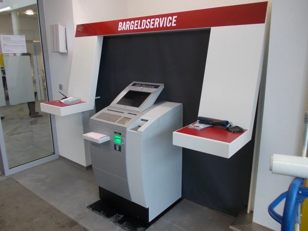 Eingebaute Nische für einen Bargeldautomaten mit roter Blende mit der Aufschrift Bargeldservice und zwei Ablagen