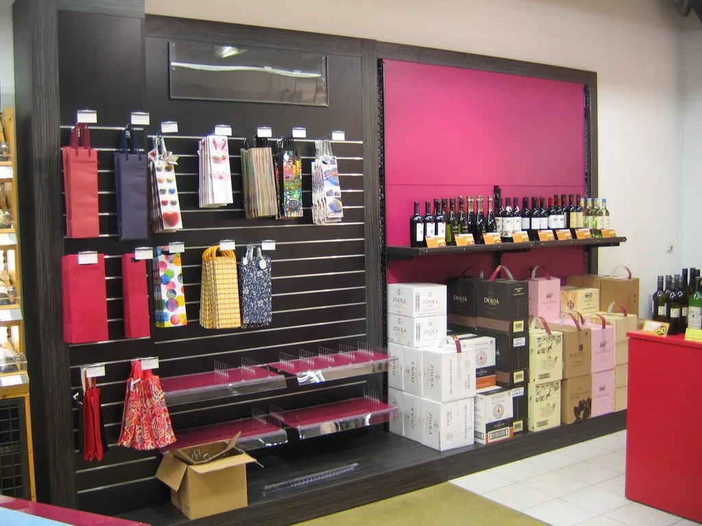 Ladeneinrichtung mit dunkler Lochwand für Geschenktaschen und pinkfarbener Rückwand mit Weinregal