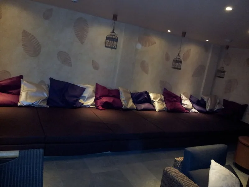 Lange dunkle Liegelandschaft mit violetten und silbernen Kissen vor einer Wand mit Blattmotiven