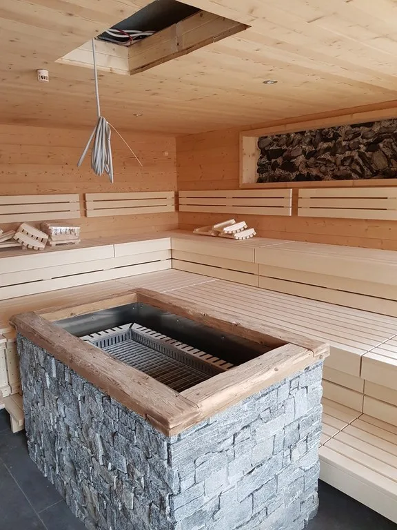 Sauna mit hellen Holzbänken und einem Ofen in einer Natursteinmauer, die Kabel an der Decke noch offen